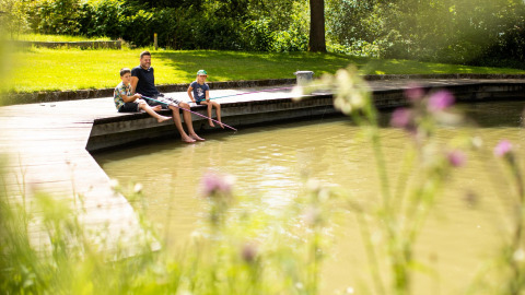 Gezin zit te vissen aan een vijver op een zonnige dag tijdens een glampingvakantie in het groen.