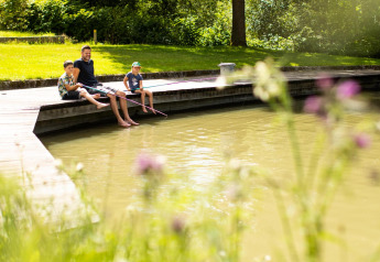 En familie nyder fiskeri ved en dam på en solrig dag under et glampingophold i naturen.