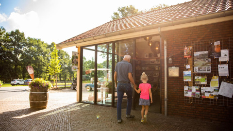 Een oudere man en een meisje wandelen hand in hand het Wood Cottage binnen bij Holiday park De Witte Berg.