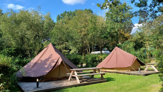 Twee Glamptent GT tenten met picknicktafels in Holiday Park BreeBronne, Nederland, omgeven door groen.