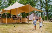 Deux filles jouent devant un lodge Glamptent GT au Holiday Park BreeBronne aux Pays-Bas, adulte au fond.