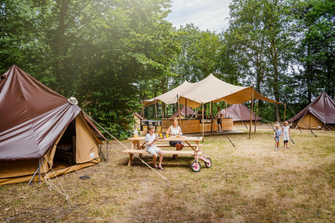 Familia disfruta acampando en Glamptent GT en Holiday Park BreeBronne, Países Bajos, rodeada de tiendas.