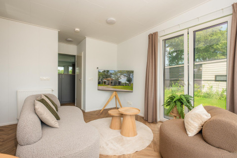 Soggiorno accogliente presso Wellness Lodge con divani moderni, tavolini in legno e vista giardino a Vakantiepark Hölte.
