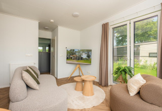 Soggiorno accogliente presso Wellness Lodge con divani moderni, tavolini in legno e vista giardino a Vakantiepark Hölte.