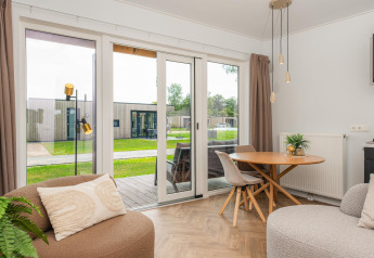 Helles Wohnzimmer in einer Wellness-Lodge mit Blick auf Terrasse und Grünfläche im Ferienpark in Holland.