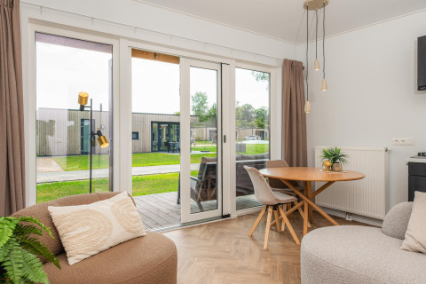 Lichte leefruimte in een Wellness Lodge met modern interieur, terras en zicht op groene grasvelden.