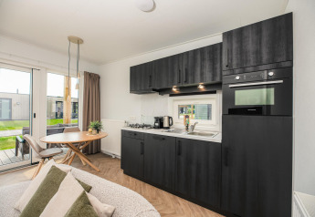 Moderne wellness-lodge med mørkt køkken, spiseplads og udsigt til terrasse i Vakantiepark Hölte, Holland.