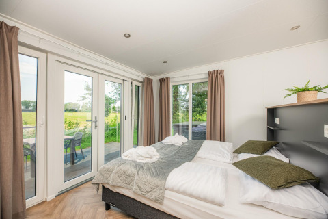 Lichte slaapkamer in Wellness Lodge met tweepersoonsbed, grote ramen en zicht op terras in Nederland.