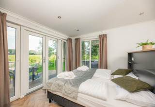 Helles Schlafzimmer in der Wellness Lodge mit Doppelbett, Fenstern und Blick auf Terrasse in den Niederlanden.