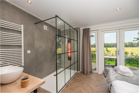 Habitación de lodge wellness moderna con ducha, cama y vista al jardín en Wellness Lodge con jacuzzi y sauna en Holanda.