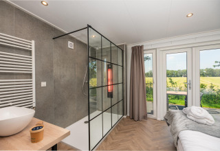 Habitación de lodge wellness moderna con ducha, cama y vista al jardín en Wellness Lodge con jacuzzi y sauna en Holanda.