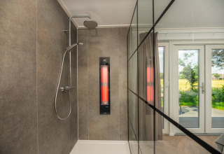 Doccia moderna con parete in vetro e pannello a infrarossi, vista giardino alla Wellness Lodge, Vakantiepark Hölte.
