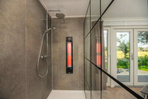 Moderne douche met glazen wand en infraroodpaneel met tuinzicht bij Wellness Lodge, Vakantiepark Hölte.