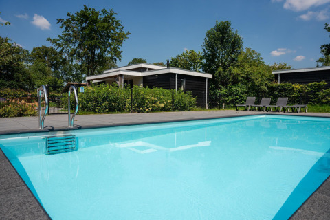 Piscina exterior junto a alojamiento glamping moderno con tumbonas y vegetación verde en un día soleado