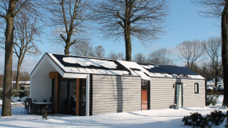 Ecovilla-Lodge im verschneiten Holiday Park Ackersate in den Niederlanden, umgeben von Bäumen.