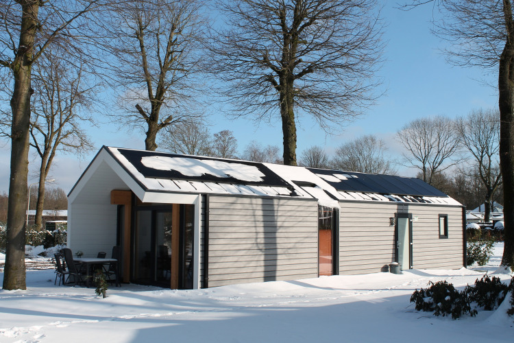 Ecovilla lodge in a snowy landscape at Holiday Park Ackersate in the Netherlands, surrounded by trees.
