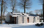Ecovilla-Lodge im verschneiten Holiday Park Ackersate in den Niederlanden, umgeben von Bäumen.