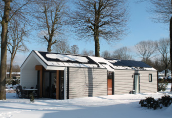 Ecovilla-lodge in een besneeuwd landschap bij Vakantiepark Ackersate in Nederland, omgeven door bomen.