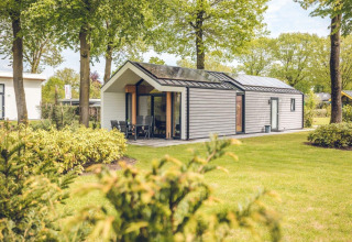 Lodge moderno llamado Ecovilla en Holiday park Ackersate, Países Bajos, rodeado de césped y vegetación.