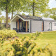 Moderne lodge ved navn Ecovilla i Holiday park Ackersate i Holland, omgivet af grønne træer og buske.