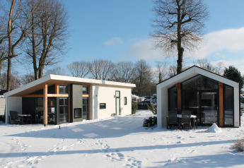 Due moderni lodge Ecovilla all’Holiday park Ackersate, Paesi Bassi, immersi nella neve e al sole.