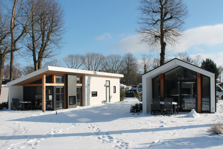 Two modern lodges called Ecovilla at Holiday park Ackersate, Netherlands, surrounded by snow and sunlight.