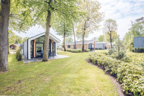 Ecovilla-lodge bij Holiday park Ackersate in Nederland, omgeven door grasvelden en groene bomen.