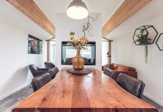 Modern lodge dining area at Ecovilla, Holiday park Ackersate, Netherlands, with wood table and plants.