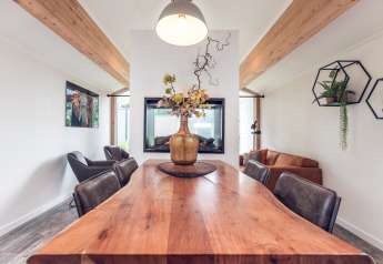 Modern lodge dining area at Ecovilla, Holiday park Ackersate, Netherlands, with wood table and plants.