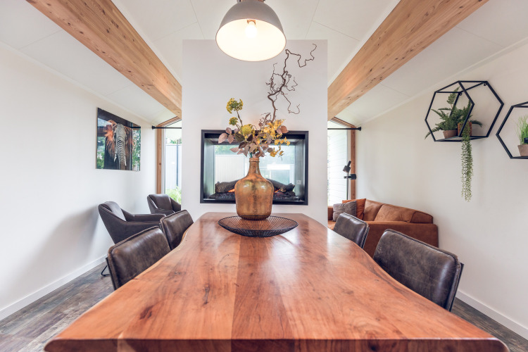 Modern lodge dining area at Ecovilla, Holiday park Ackersate, Netherlands, with wood table and plants.