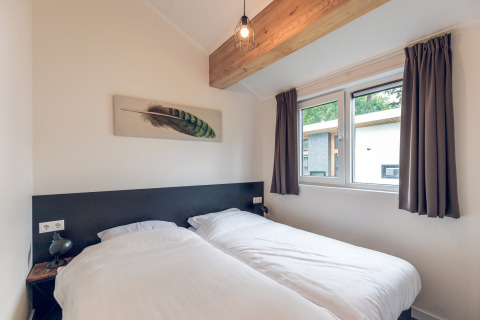 Camera da letto nell’Ecovilla dell’Holiday park Ackersate, Paesi Bassi, con due letti singoli e finestra.