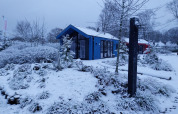 Cabaña de caza con sauna cubierta de nieve en el parque Holiday Ackersate, Países Bajos, rodeada de árboles.