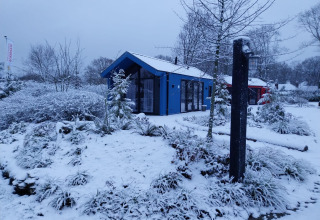 Sneeuwbedekte jachthut en sauna bij Holiday park Ackersate in Nederland, omringd door winterse bomen.