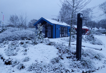 Sneklædt jagthytte og sauna ved Holiday park Ackersate i Holland, omgivet af vinterlige træer og buske.