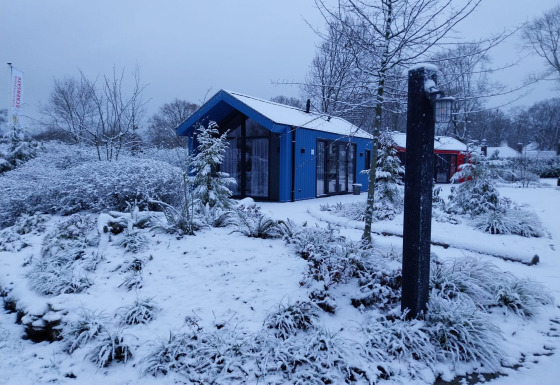 Sneklædt jagthytte og sauna ved Holiday park Ackersate i Holland, omgivet af vinterlige træer og buske.