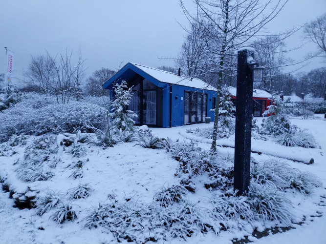 Verschneites Jagdchalet mit Sauna im Ferienpark Ackersate in den Niederlanden, umgeben von Winterlandschaft.