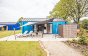 Hunting chalet with blue exterior, outdoor seating, sun loungers and sauna at Holiday park Ackersate, Netherlands.