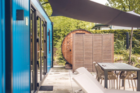 Zona exterior junto a un chalet de caza con sauna, asientos modernos y fachada azul en Holiday park Ackersate.