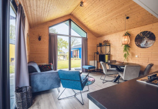 Interior de un lodge moderno con paredes de madera, grandes ventanas, sala acogedora y comedor elegante.