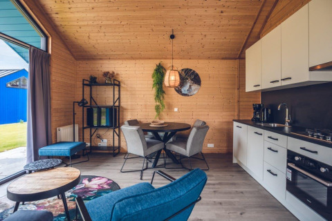 Interior moderno de cabaña con paredes de madera, mesa de comedor, sala y cocina equipada.