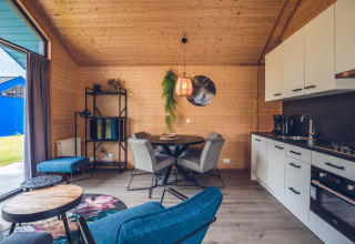 Interior moderno de cabaña con paredes de madera, mesa de comedor, sala y cocina equipada.
