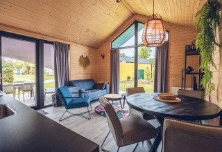 Interior de una moderna cabaña con paredes de madera, grandes ventanas y vista hacia el jardín verde.