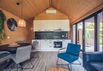 Interior de lodge moderno con cocina abierta, comedor, paneles de madera y grandes ventanales a la terraza.