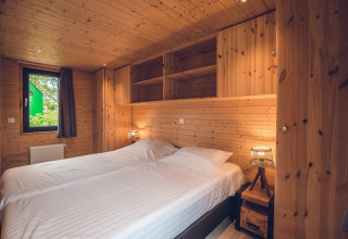Acogedor dormitorio de una cabaña con paredes y techo de madera, cama doble y ventana con cortina.