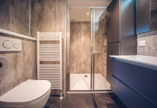 Modern lodge bathroom with walk-in shower, wall-mounted toilet, heated towel rail, and sleek storage units.