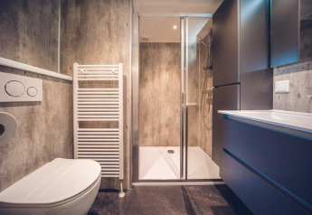 Moderne badeværelse på lodge med brusekabine, væghængt toilet og opbevaringsskabe i minimalistisk stil.