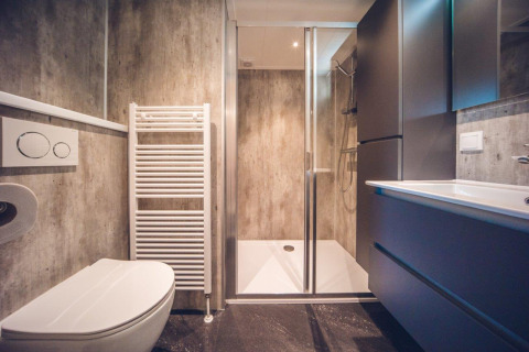 Modern lodge bathroom with walk-in shower, wall-mounted toilet, heated towel rail, and sleek storage units.