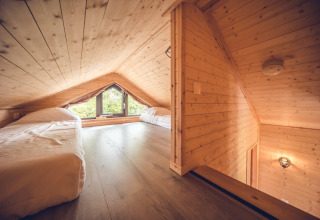 Dormitorio en altillo de una cabaña de madera con techo inclinado, dos camas individuales y ventana grande.