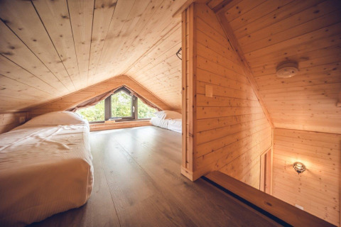 Dormitorio en altillo de una cabaña de madera con techo inclinado, dos camas individuales y ventana grande.