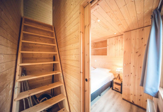 Wood-paneled lodge interior featuring a simple wooden staircase and a bedroom with a double bed and nightstand.
